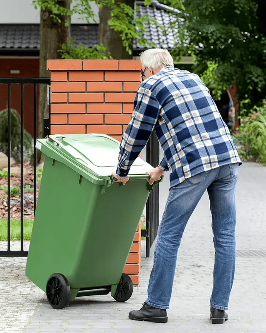 Elderly man pushing green trash bin